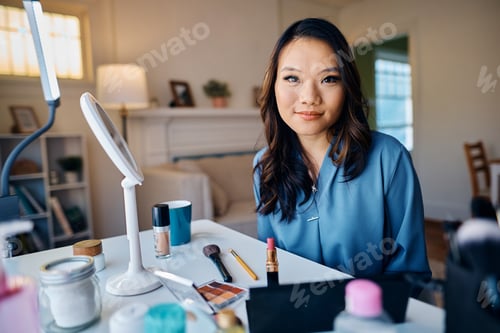 Preview: Young Asian woman doing make up at home and looking at camera.