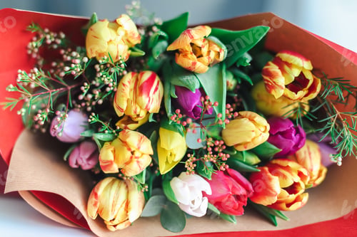Preview: A colorful bouquet of spring tulips in bright red wrapping paper lies on the table.