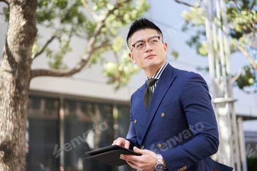 Preview: Asian businessman doing research on a tablet outside