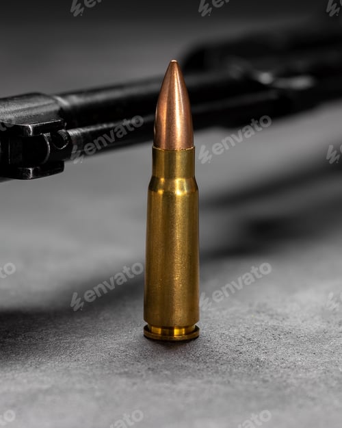Preview: Single bullet standing upright with blurred dark firearm