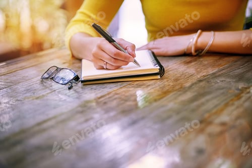 Preview: Cropped shot of a woman sitting at a table and writing in her notepad