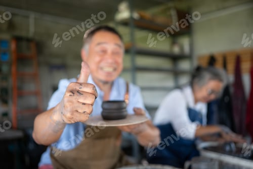 Preview: Portrait of senior craftsman working on pottery with thumb up
