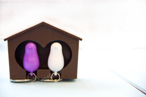 Preview: House key on a house shaped keychain on wooden table. Concept for real estate or renting home.