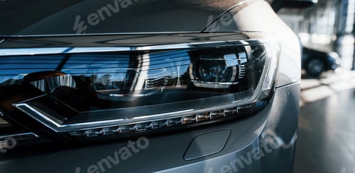 Preview: Front part of brand new modern car. Parked at showroom. Reflection in the headlights