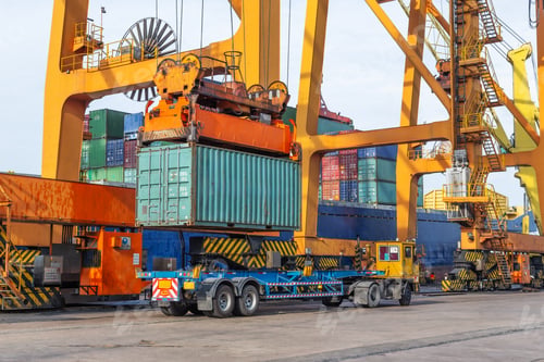 Preview: A port crane lifts a large shipping container onto a flatbed trailer