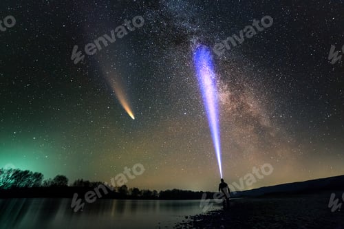 Preview: Silhouette of a man with head flashlight standing on river bank lighting a beam of light