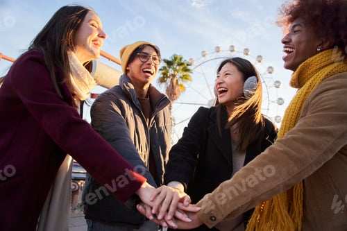Preview: Group of smiling multi-ethnic people joining hands at amusement park in sunny winter vacations.