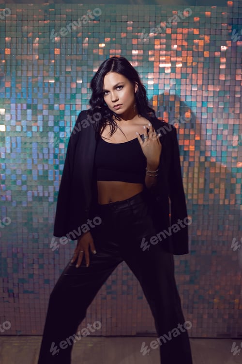 Preview: sexy young energetic woman in black suit in the studio against a background of shiny squares