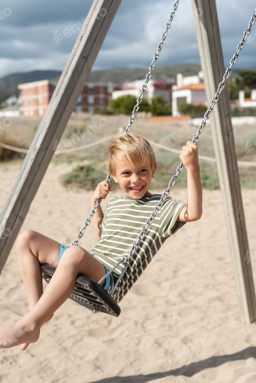 Preview: A happy boy on a swing on a sandy beach against the backdrop of apartment buildings and a stormy sky