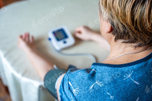 Preview: Senior woman checking blood pressure level at home, older female suffering from high blood pressure