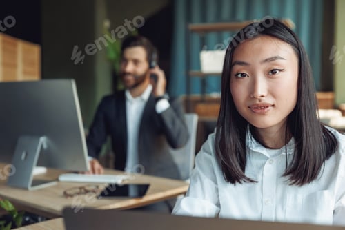 Preview: Asian businesswoman working in office and looking camera on background of colleague