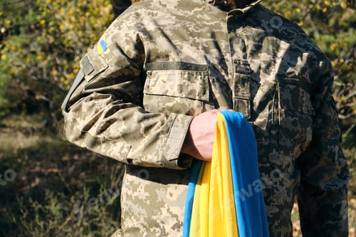 Preview: Ukrainian soldier holds in his hand the yellow-blue flag of the state