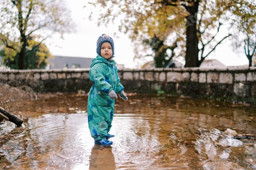 Preview: Little girl in rubber boots stands in a puddle in an autumn park. Side view