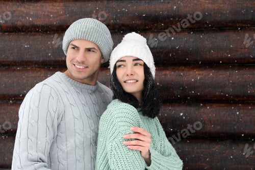 Preview: Lovely couple wearing warm sweaters and hats near wooden wall. Winter season
