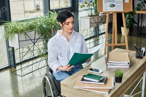 Preview: confident disabled businesswoman in wheelchair looking at her paperwork at her workplace in office