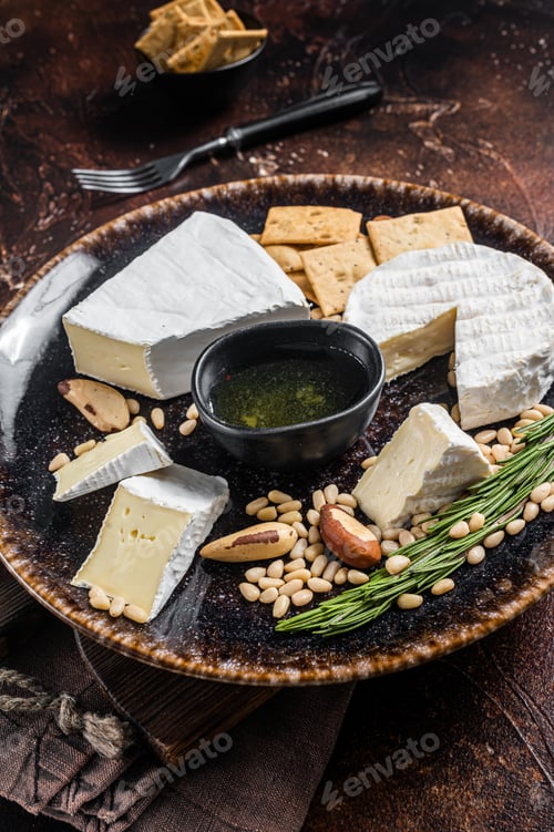 Preview: Cheese plate with brie and camembert on rustic plate with nuts and honey. Dark background. Top view