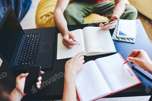 Preview: Crop students doing homework together in workplace
