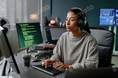 Preview: Middle Eastern Female Developer Coding on Computer Wearing Headphones in Office