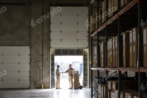 Preview: Two warehouseworkers shaking hands in the door of a loading dock in a warehouse.