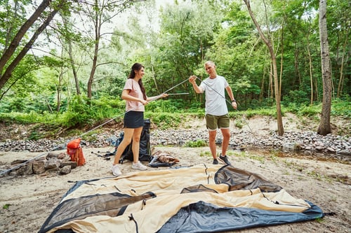 Preview: Cheerful young couple fixing tent in wood