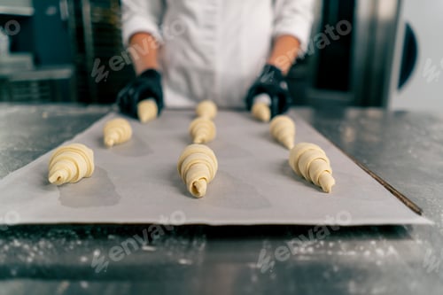 Preview: baker's hands placing shaped uncooked croissants on a baking sheet with parchment baking in the oven