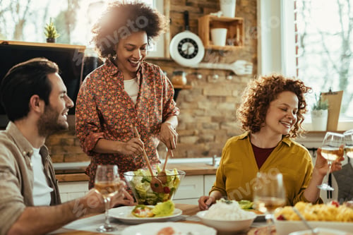 Preview: Happy black woman serving salad while having lunch with her friends at home.