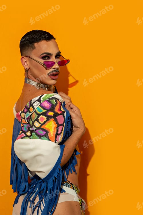 Preview: Portrait of beautiful fashionable drag queen in multicolored costume with yellow background.