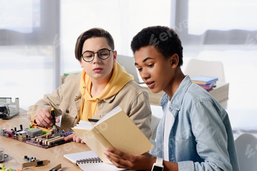 Preview: multicultural teen boys reading book about soldering motherboard at home