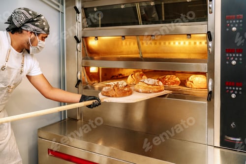 Preview: Latino baker putting bread in the oven with gloves and a mask
