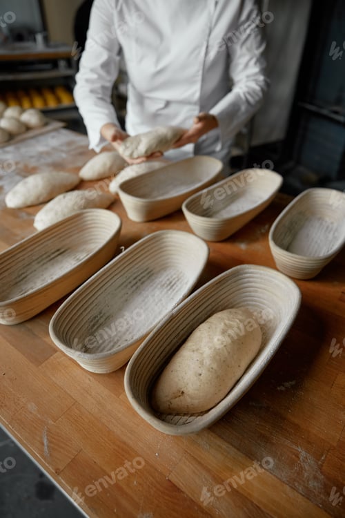 Preview: Closeup baker forming baguettes from raw dough while working in bakery