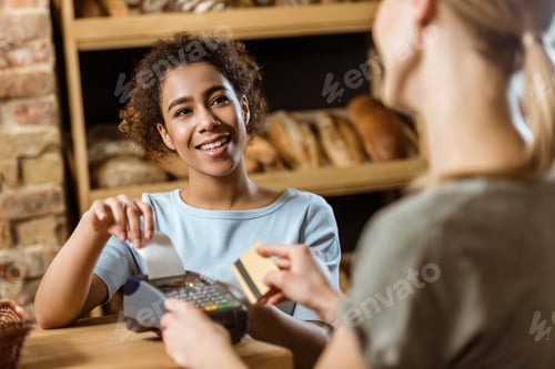 Preview: happy cashier with pos terminal receiving purchase from client at pastry store
