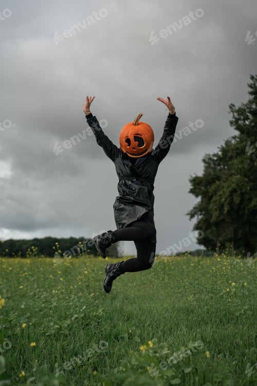 Preview: Vertical shot of a young woman wearing a pumpkin on her head in the forest