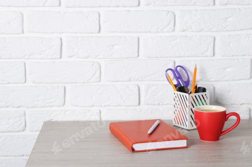 Preview: Different stationery and coffee on wooden office table near white brick wall