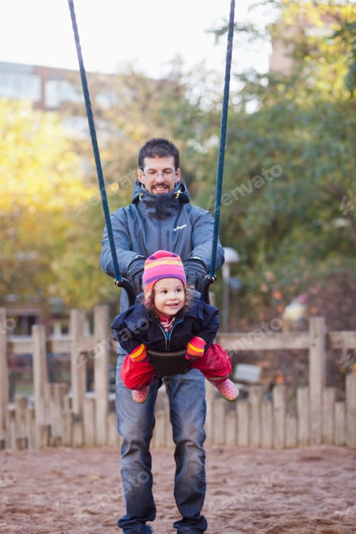 Preview: Father pulling swing with girl at playground in park