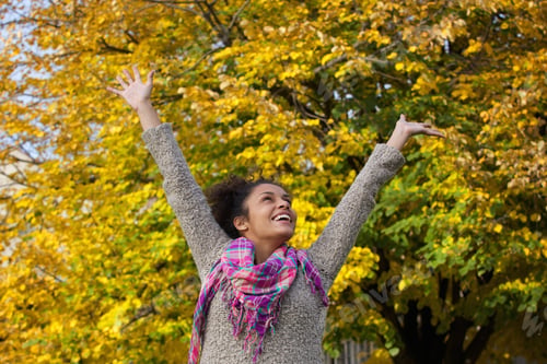 Preview: Carefree young woman enjoying autumn with arms raised