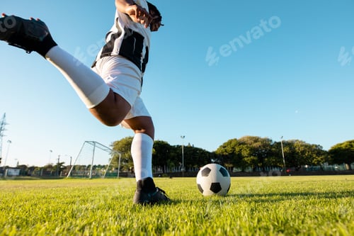 Preview: African American man kicking soccer ball on field wearing striped jersey and cleats, copy space