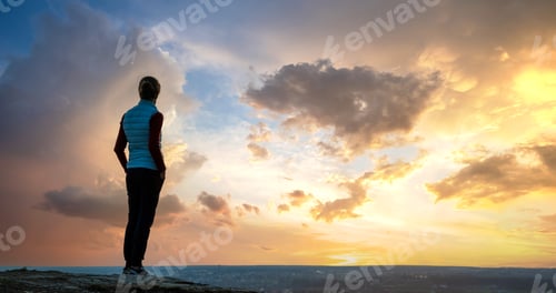 Preview: Silhouette of a woman hiker standing alone enjoying sunset outdoors.