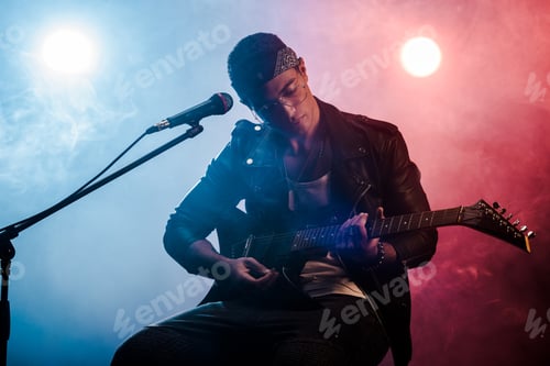 Preview: focused male musician playing on electric guitar near microphone on stage during rock concert