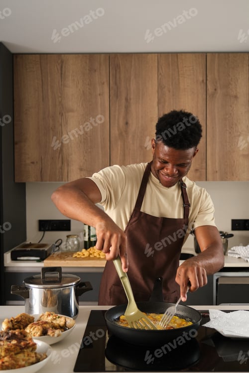 Preview: Young black man frying plantains slices.