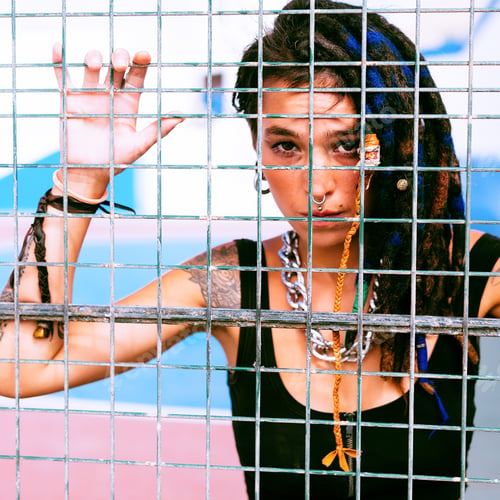 Preview: Girl with dreadlocks behind the metal grid on sports ground