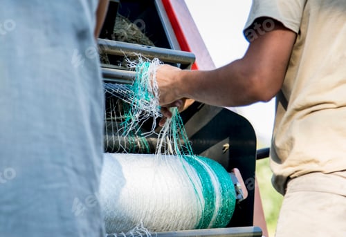 Preview: Cropped shot of two male farmworkers untangling netting in hay baler