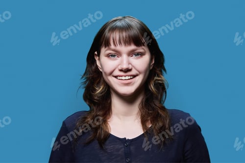 Preview: Headshot portrait of young female looking at camera on blue background