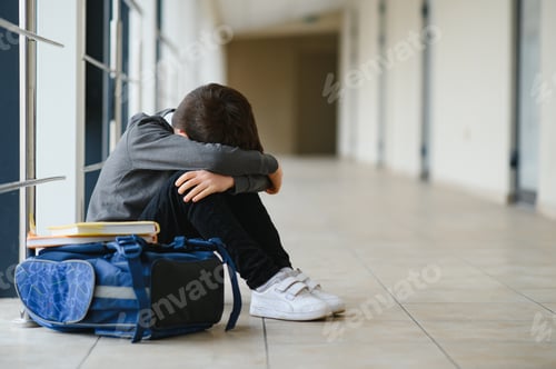 Preview: Little boy sitting alone on floor after suffering an act of bullying while children run