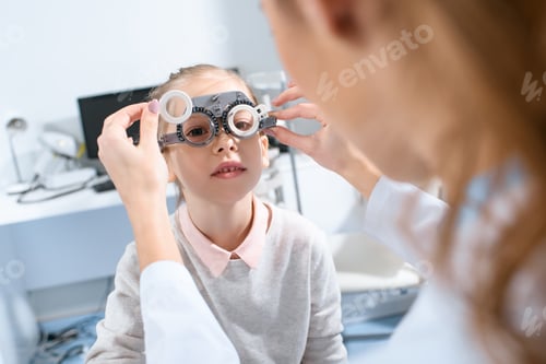 Preview: selective focus of ophthalmologist examining kid eyes with trial frame in clinic