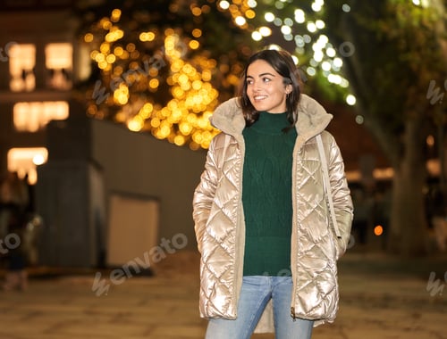 Preview: Woman in winter coat looking away and smiling while standing outdoors.