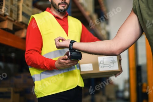 Preview: Closeup of modern man paying via smartwatch while buying package in warehouse - Industrial worker