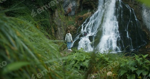 Preview: Woman traveler enjoying waterfall in Austria. Traveling in the mountains forest in rainy day