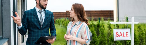Preview: panoramic shot of handsome bearded broker holding clipboard and gesturing near attractive woman