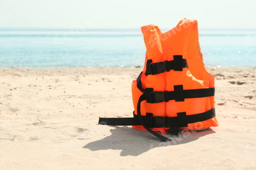 Preview: Orange life jacket on sandy beach near sea. Emergency rescue equipment