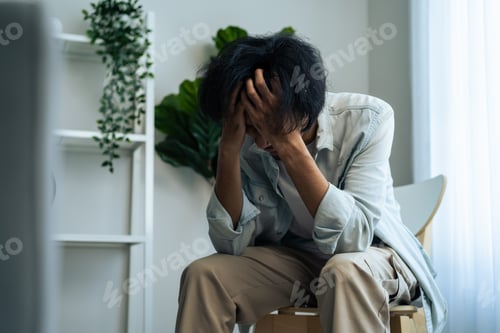 Preview: Asian young upset depressed man sitting alone in living room at home.